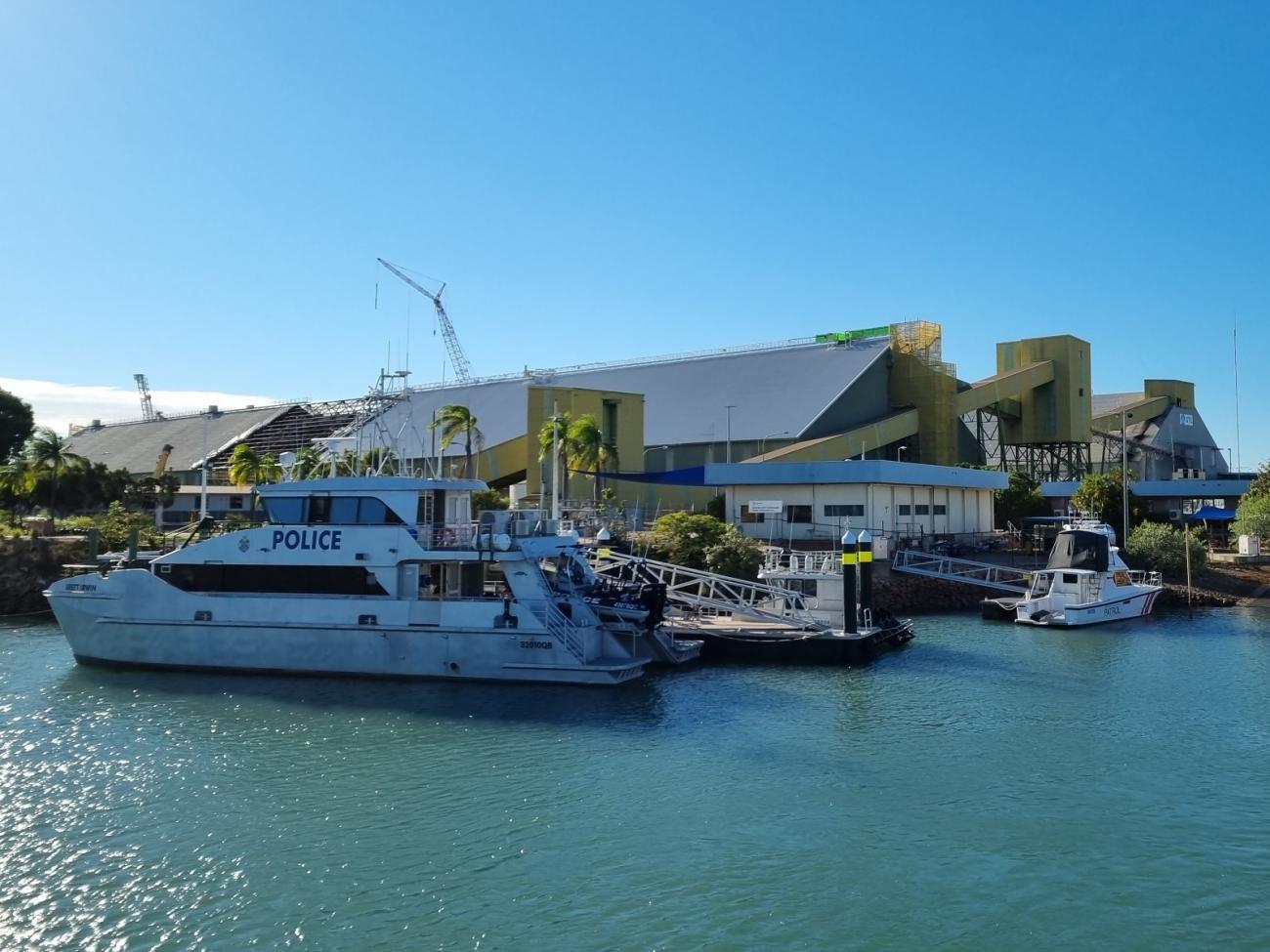 Townsville Sugar Terminal at the water's edge, featuring PERMALITE® aluminium roofing, with a police boat docked in blue water in the foreground and other boats at nearby docks.